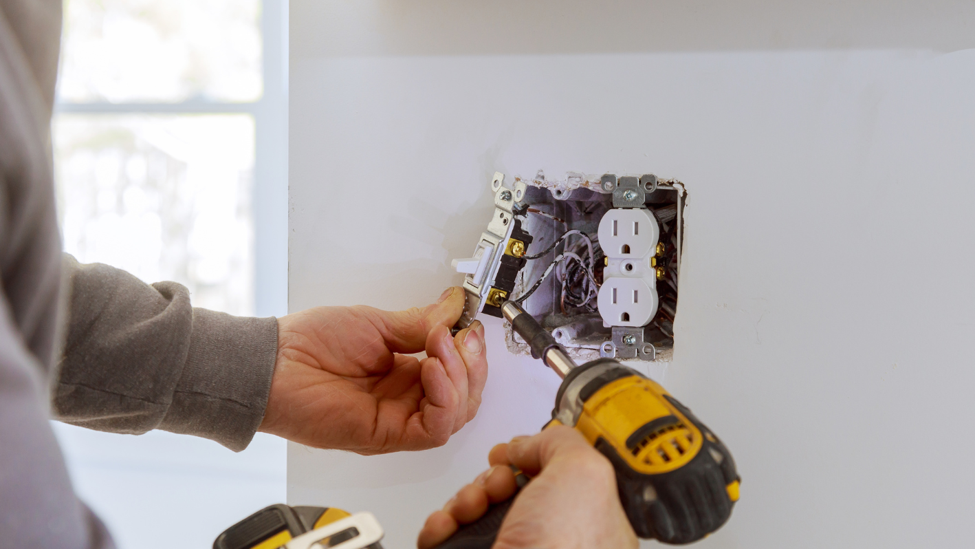 A man is using a screwdriver to fix a light switch